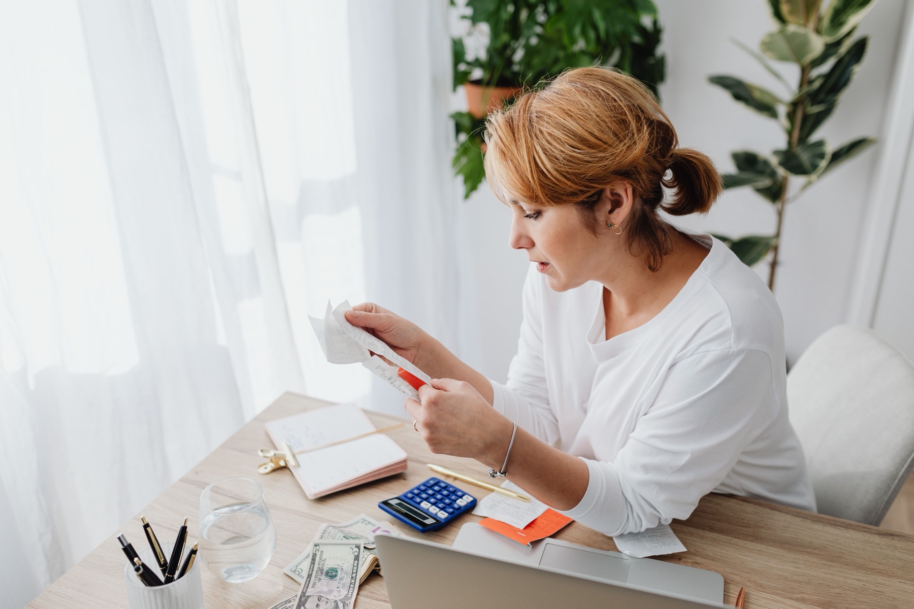 Illustrative stock photo of a woman reviewing receipts at a desk with a calculator and laptop